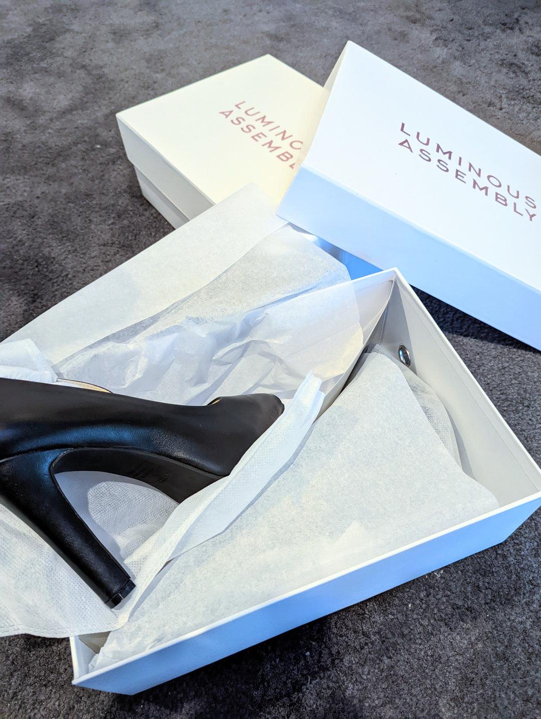 Black high heels with a Luminous Assembly shoe box